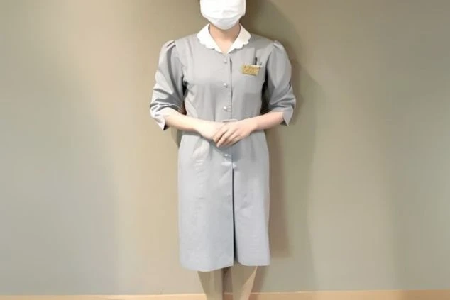 白い襟がアクセントになったグレーのワンピースタイプの制服を着用した客室係スタッフ。リゾートバイトで客室清掃やベッドメイク、客室補助の仕事に興味がある方に訴求する画像。