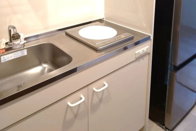 居室内のキッチン。一口IHクッキングヒーターとシンク、引き出しがあり、横に冷蔵庫。