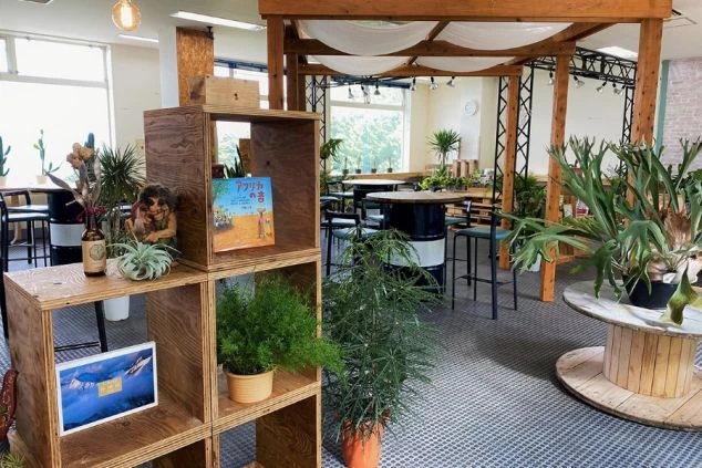 木製ボックスの棚や観葉植物がセンス良く配置された、開放的なフリースペース。ドラム缶を再利用したテーブルや天蓋のような白い布が、遊び心のあるナチュラルでモダンな空間を演出している。