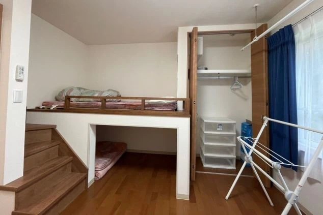 ワクトリの社員が出張で撮影した、リゾートバイトの寮の部屋の画像。ロフトベッドと下段にも寝具が置かれた二層式の空間で、クローゼットや物干しスタンドも見える。