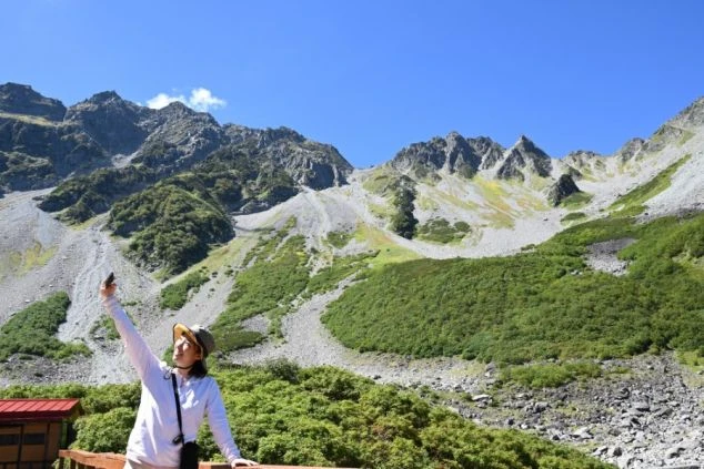 雄大な山々を背景に自撮りを楽しむ女性。登山やハイキングも楽しめる山のリゾートバイト。