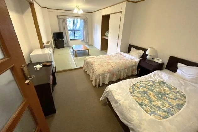 手前に2台のシングルベッド、奥に畳の小上がりがある和洋室。花柄のベッドカバーが印象的で、広々とした造りになっている。