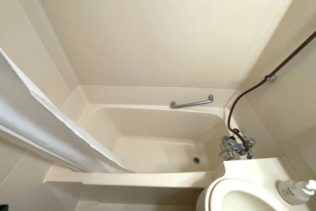 クリーム色のシンプルなユニットバスの俯瞰写真。浴槽と洗面台、温水洗浄便座付きのトイレが配置されている。