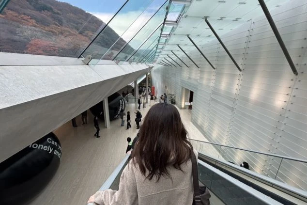 神奈川県箱根町にある「ポーラ美術館」の美しい建築デザインと、エスカレーターから外の景色を眺める女性の後ろ姿の写真。
