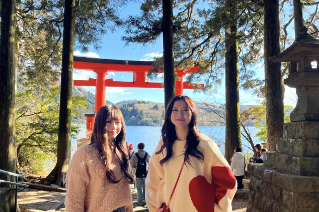 箱根・芦ノ湖の平和鳥居をバックに笑顔で並ぶ2人の女性スタッフ。リゾートバイトの休日や休憩中に観光スポットを巡る、楽しく充実したライフスタイルの様子