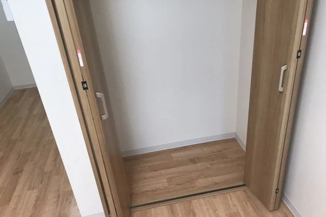 寮の居室にあるクローゼット（収納）。観音開きのドアを開けた状態の内側で、奥の壁は白く、床はフローリング。