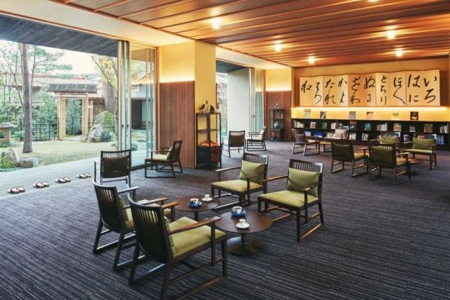 石川県加賀市の山代温泉にある温泉旅館の館内の画像。和モダンなインテリアと、壁一面に広がる「いろは歌」の書、そして美しい日本庭園を望む開放的なラウンジスペース。
