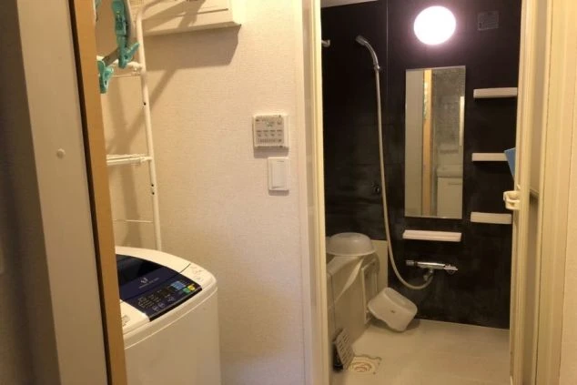 リゾートバイトの寮のバスルームと洗濯機が写っている画像。バスルームは黒いタイル張りで、洗濯機は縦型である。リゾートバイトの寮の共用スペースの画像。