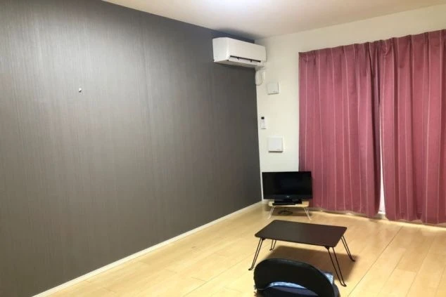 リゾートバイトの寮の部屋の画像。床はフローリングで、テレビと座卓、そしてピンク色のカーテンが特徴的である。リゾートバイトの寮の部屋の画像。