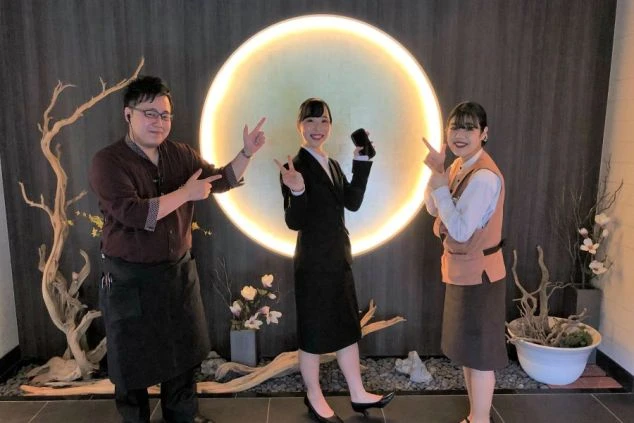 月のような丸い間接照明が美しい和モダンなリゾートホテルのロビーで、笑顔を見せるフロントスタッフたちの写真。制服に身を包んだ男女のスタッフが仲良くポーズをとる、活気ある職場の日常風景。