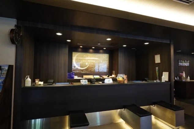 モダンで高級感あふれるリゾートホテルのフロントレセプションの画像。落ち着いたダークブラウンのウッド調カウンターと、背面に飾られた黄金色の和モダンなアートが上質な空間を演出。