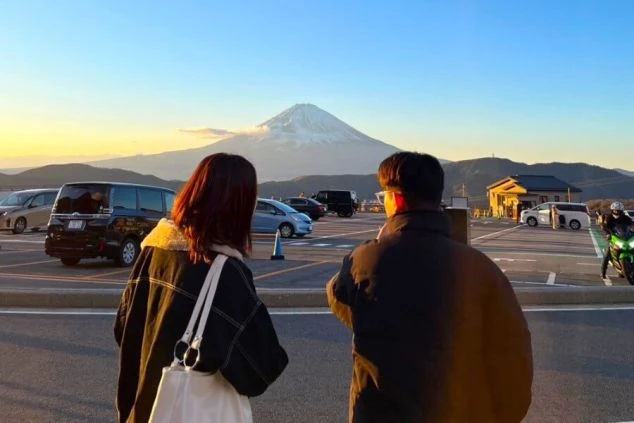 夕暮れ時に雪化粧をした富士山を正面に望む、リゾートバイトの男女スタッフの後ろ姿の画像。箱根や富士五湖エリアの展望スポットから、神々しく輝く富士の絶景を眺めてリフレッシュする休日のひととき。
