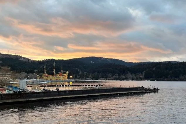 神奈川県箱根町の芦ノ湖に浮かぶ、ライトアップされた黄金の「箱根海賊船」と夕焼けに染まる空の画像。湖畔の桟橋から望む、静かな湖面と雄大な外輪山のシルエット。