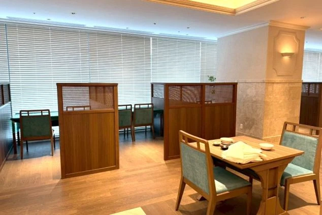 木目調のパーテーションで区切られた、落ち着いた雰囲気のレストラン内観。ミントグリーンの椅子が配された清潔感のあるテーブル席が並び、ブラインド越しに柔らかな光が差し込む上質な食事空間。