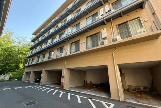寮として利用されている多層階のマンション風の建物。1階部分は駐車場になっており、各階のベランダにはエアコンの室外機が並んでいます。