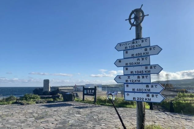 北海道利尻島の「沓形岬公園」にある、サハリンや礼文島、稚内など各都市への距離を示すユニークな青い標識の画像。青空と日本海をバックに、最果ての地を感じさせるノスタルジックな風景。