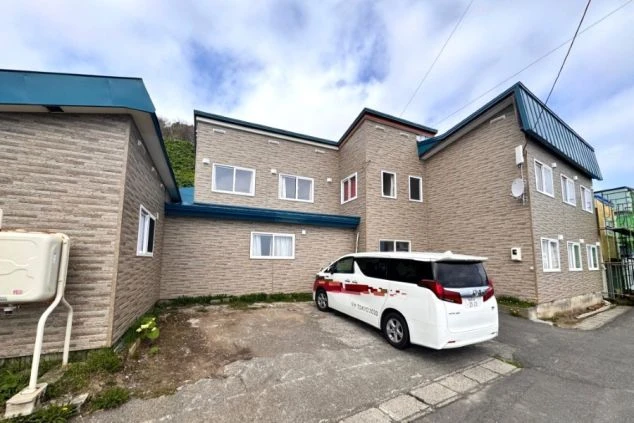 礼文島の寮外観写真。駐車場には車が停まっており、寮からは海が見える。