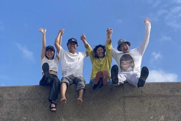 澄み渡る青空の下、4人の男女が手を繋いで笑顔でバンザイ！ワクトリで出会った一生の仲間と過ごす、最高のリゾートバイトの休日です。