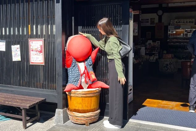 リゾートバイトの休日に飛騨高山の名物さるぼぼと記念撮影を楽しむ女性