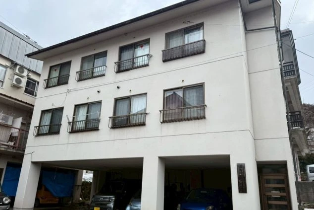 リゾートバイトの寮の外観画像。白を基調とした三階建ての建物。