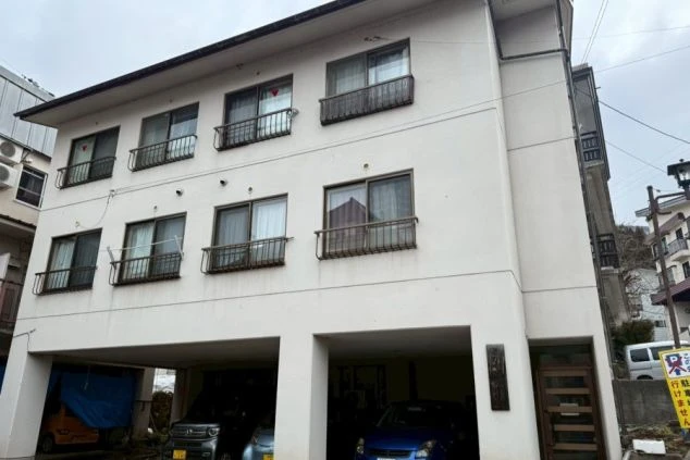 リゾートバイトの寮の外観画像。白を基調とした三階建ての建物。