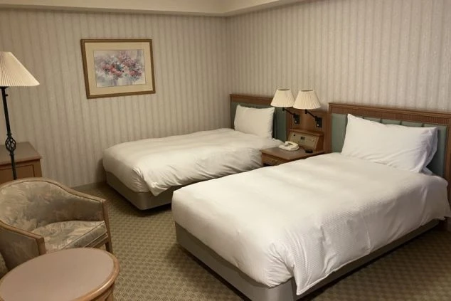 リゾートバイトの客室寮(相部屋)の画像。ツインベッド、ソファ、テーブルがある洋室。