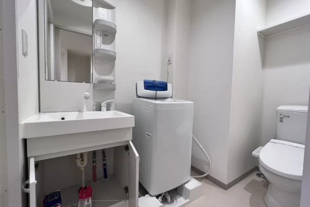 洗面台とトイレ、洗濯機がコンパクトに配置されたリゾートバイトの寮の水回りスペースの画像。設備が新しいことをアピール。