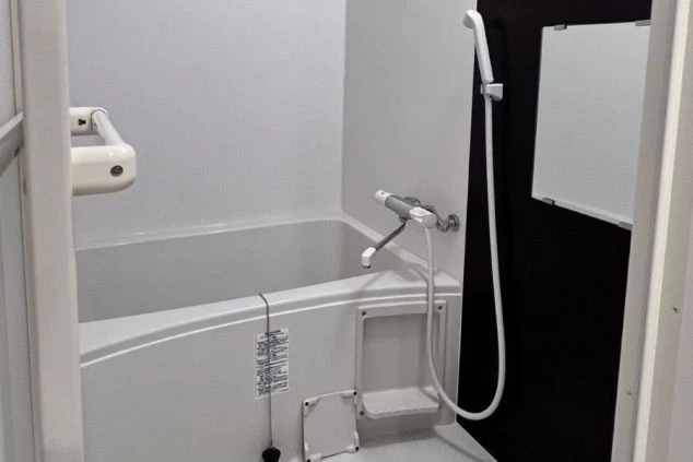 シンプルで清潔なリゾートバイトの寮のユニットバスまたは浴室の画像。シャワーと浴槽が完備されていることを示す。